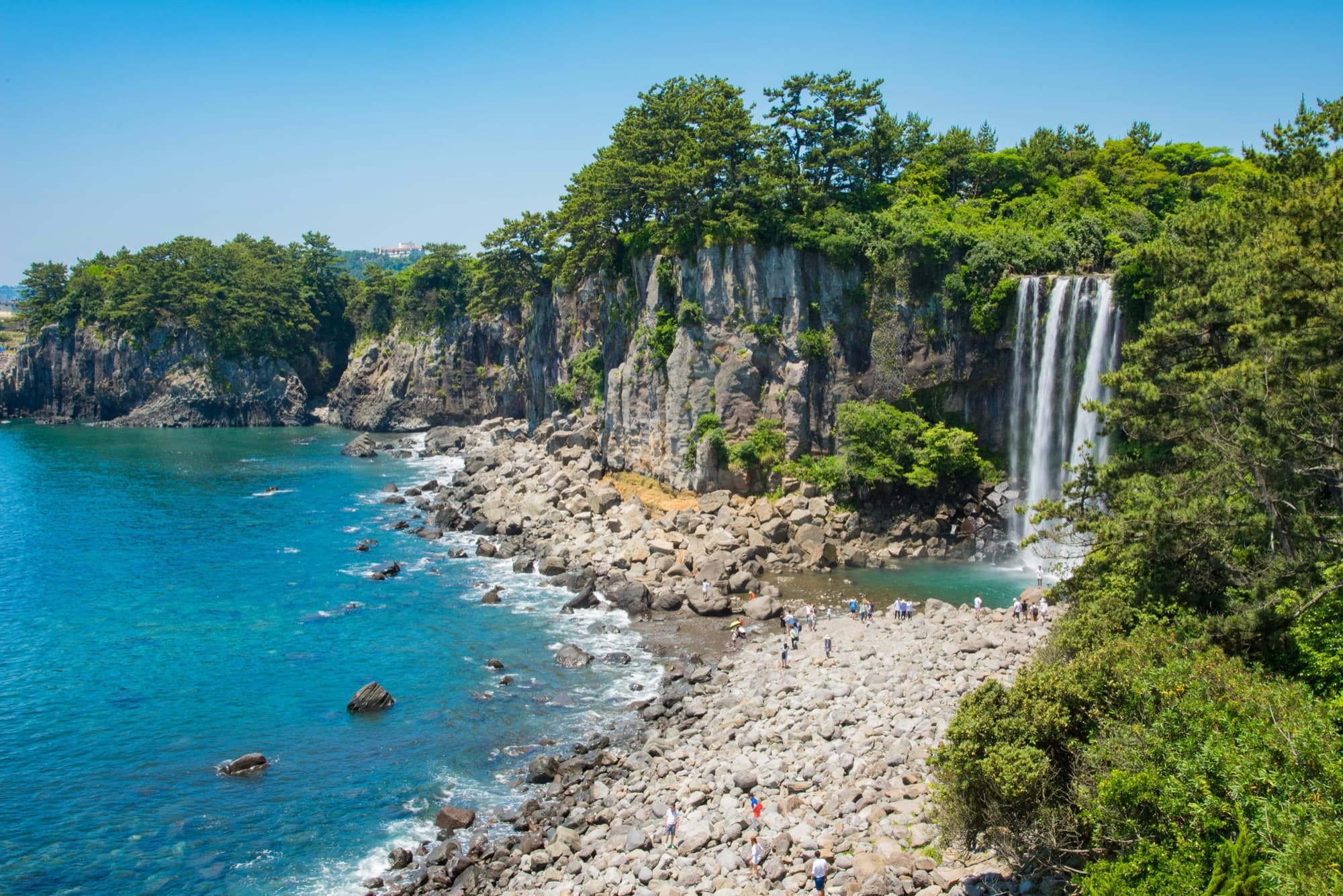 A waterfall dropping onto a rocky coastline on Jeju island, with cliffs and turquoise water