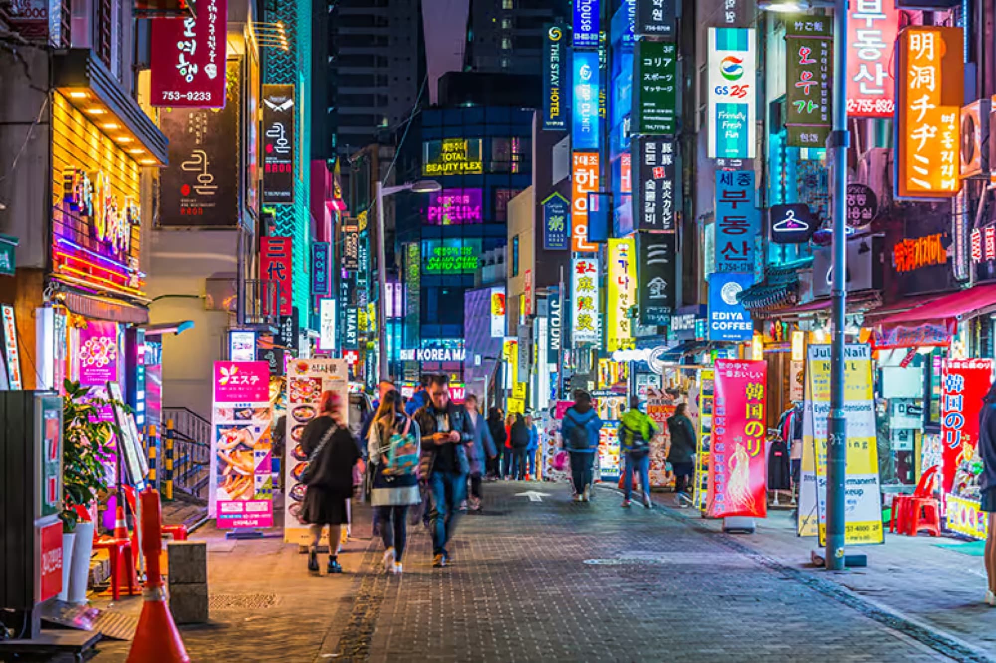 A neon-lit shopping street at night in Seoul, crowded with signs and pedestrians