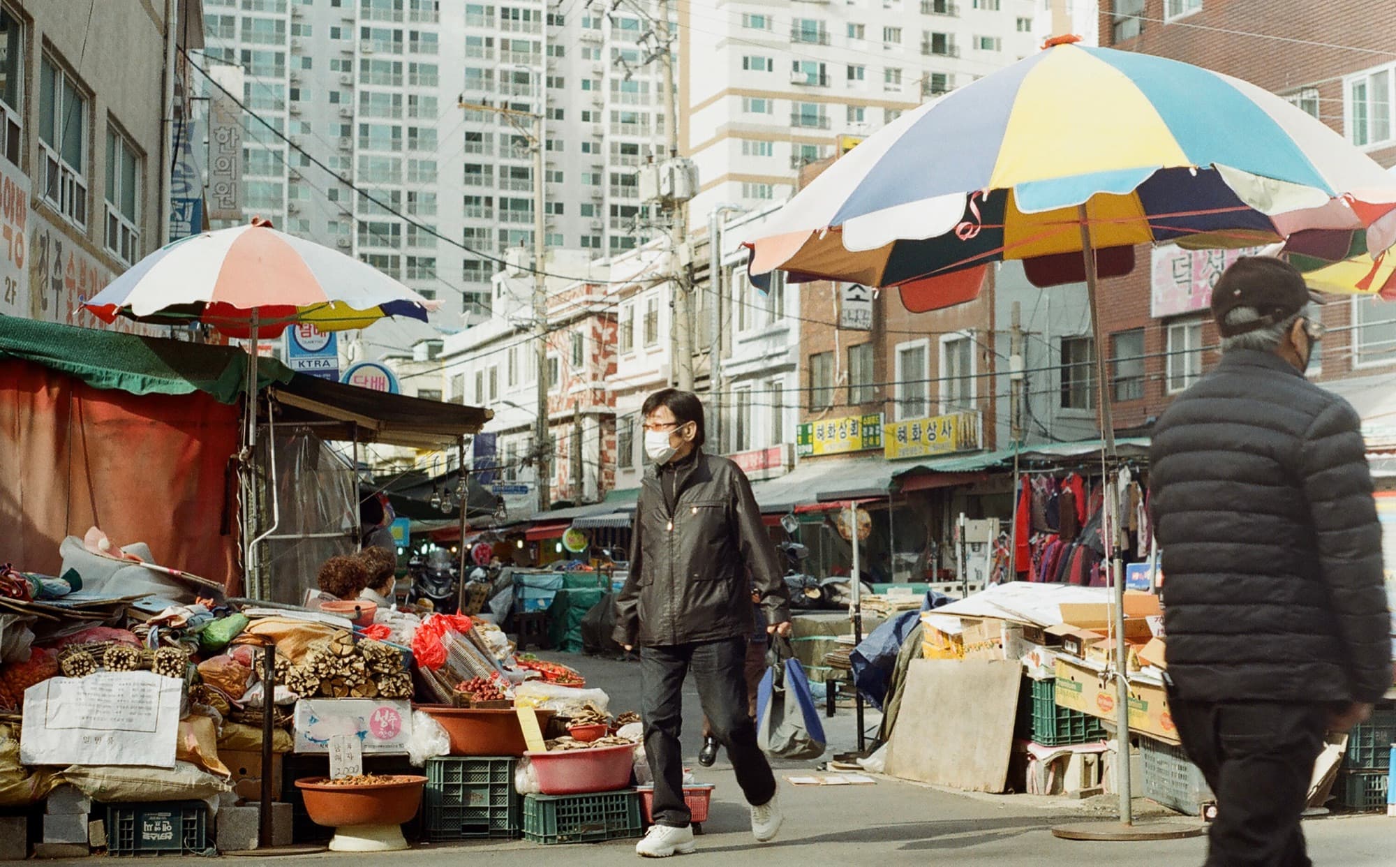 A pedestrian street market in Seoul, market umbrellas in the foreground and apartment towers behind